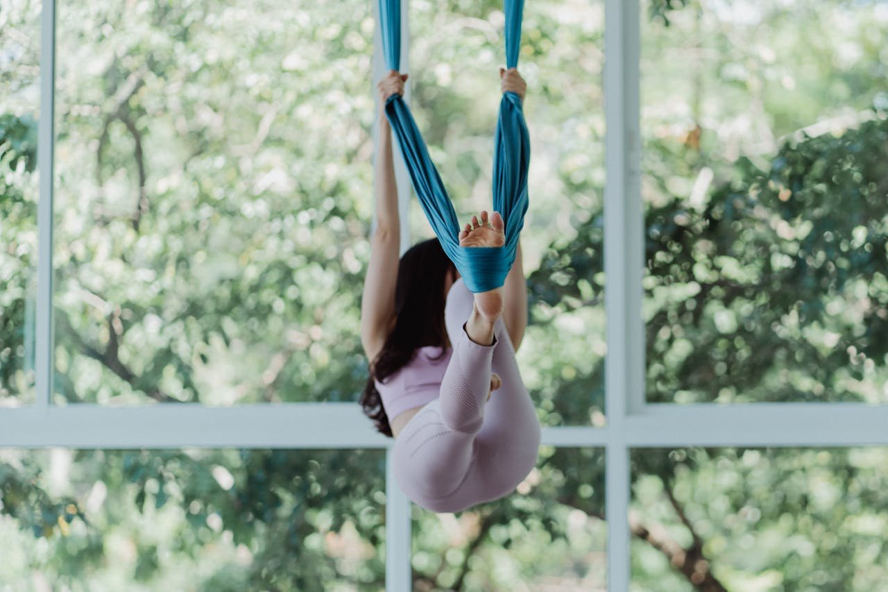 project-02-d A woman performs aerial yoga with fabric near a large window, surrounded by nature.