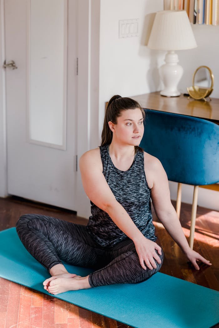 A woman practicing a seated yoga pose at home on a turquoise mat for relaxation and health.