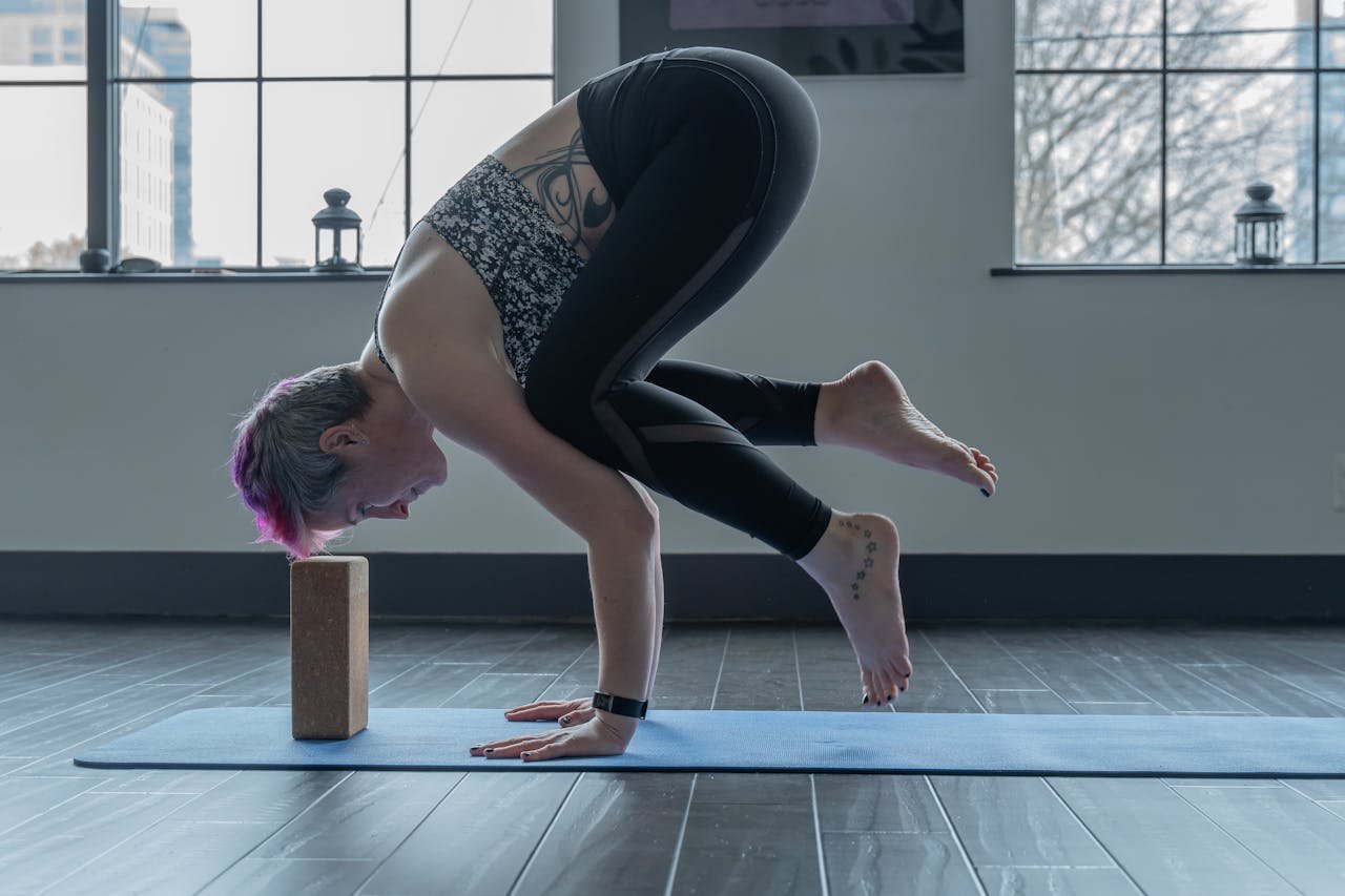 services-01 Woman performs advanced yoga pose indoors using a brick for balance, showcasing strength and flexibility.